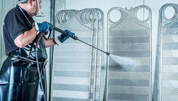 A man in blue gloves is using a hose to clean metal.